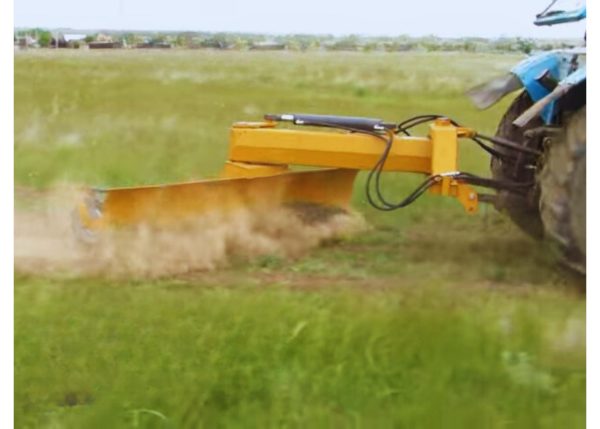 A side view of a multi-purpose rear blade attached to a farm tractor, curved and in action on farm land.