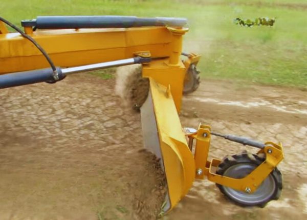 A multi-purpose rear blade attached to a farm tractor, viewed from the left side while leveling the farmland.