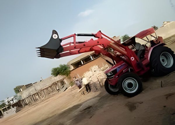 Murshid Farm Industries Implement HYDRAULIC FRONT END LOADER in full loading position, lifting hay bales onto a truck.