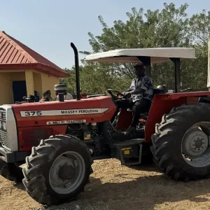 Massey Ferguson MF 375 tractor manufactured by Millat Tractors Pakistan, fitted with canopy and attached tipping trailer, shown in a working farm yard