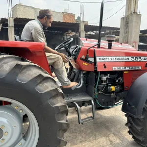 Millat Massey Ferguson MF 385 4WD 85 HP tractor left side view with operator seated and driving in outdoor factory yard