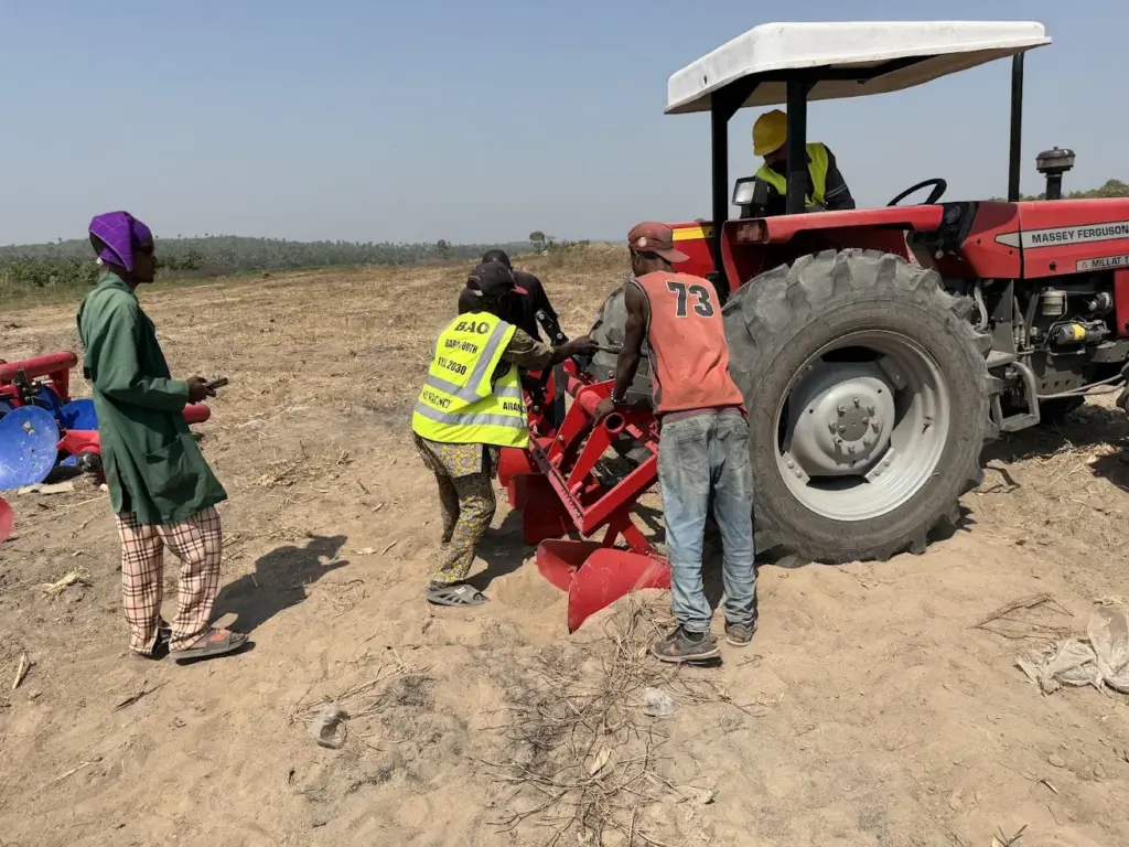 Tractor and soil-working implement in a field Red tractor with a soil-working implement and people in a cultivated field
