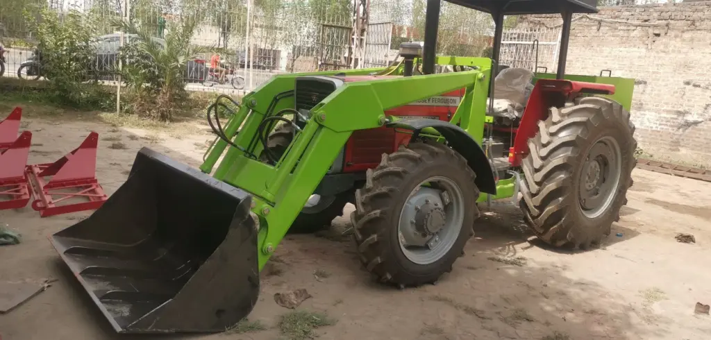 Tractor fitted with a front loader Red tractor with a green front loader and black bucket in a yard